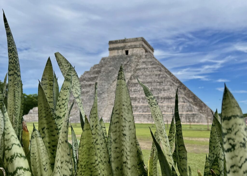 Chichen Itza’s Kukulkan Pyramid with green plants in the foreground and blue sky above