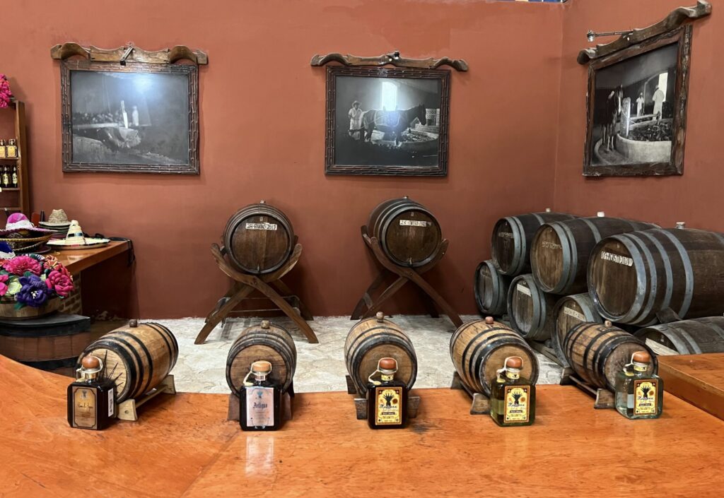 Tequila barrels and bottles displayed on a wooden counter in a rustic tasting room with vintage photos on the wall