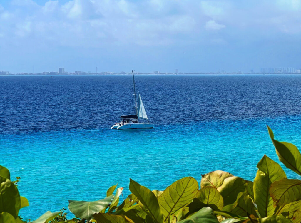 Visiting Cancun on a sailboat on vibrant turquoise waters, framed by lush green leaves