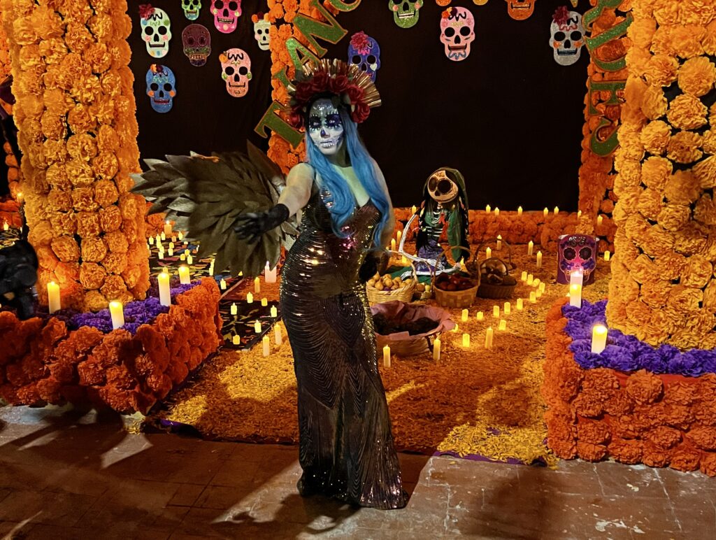 A girl dressed as La Catrina standing in front of the altar during the Day of the Dead in Mexico